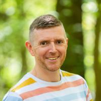 man wears striped top with green nature background